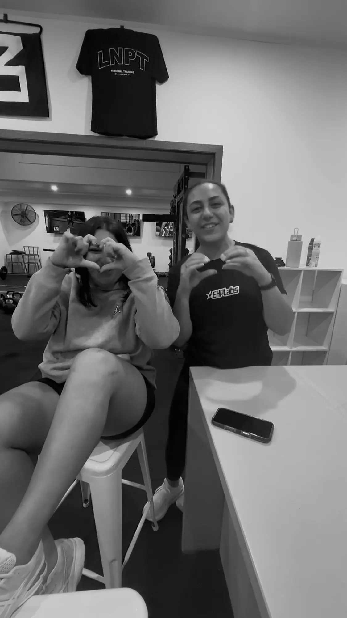 Two LNPT members make heart shapes with their hands in the studio.