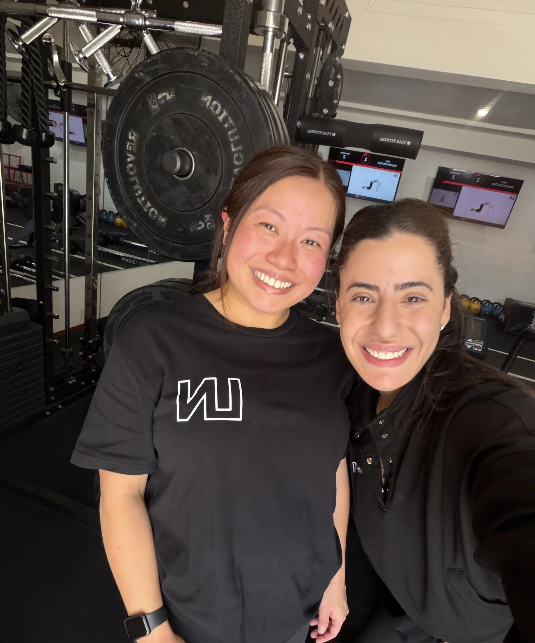 An LNPT coach and member smile together beside strength equipment.