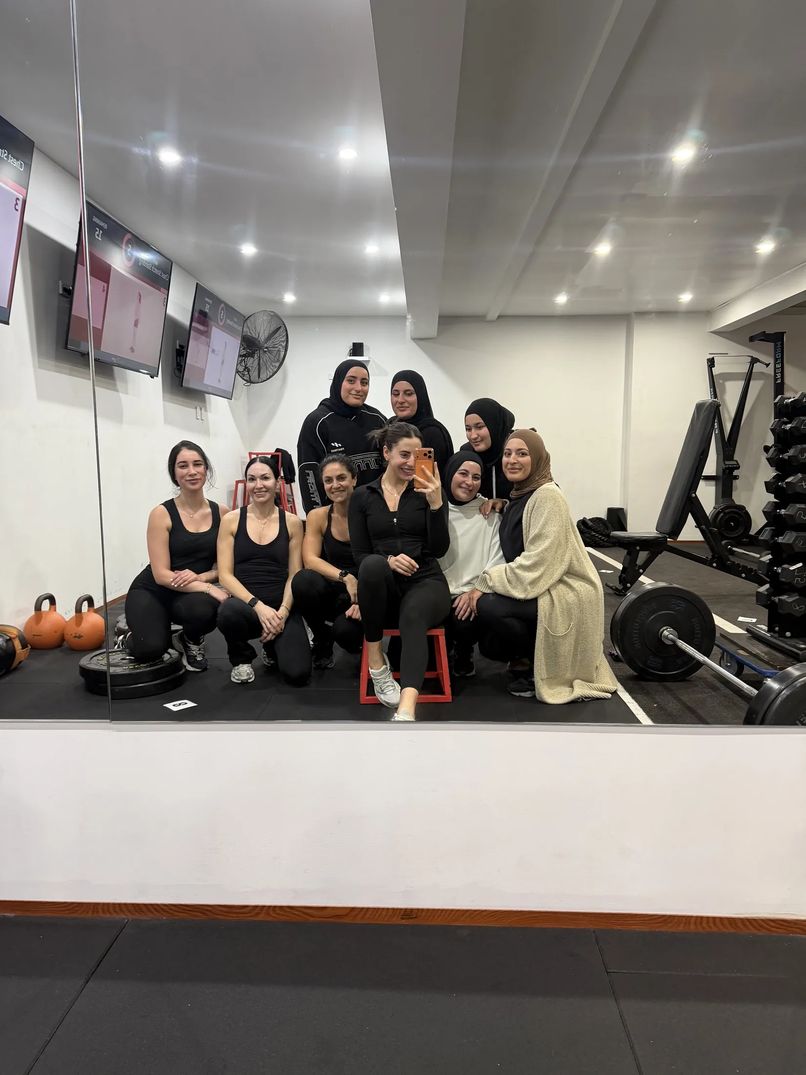 LNPT women pose together for a group mirror selfie in the training studio.
